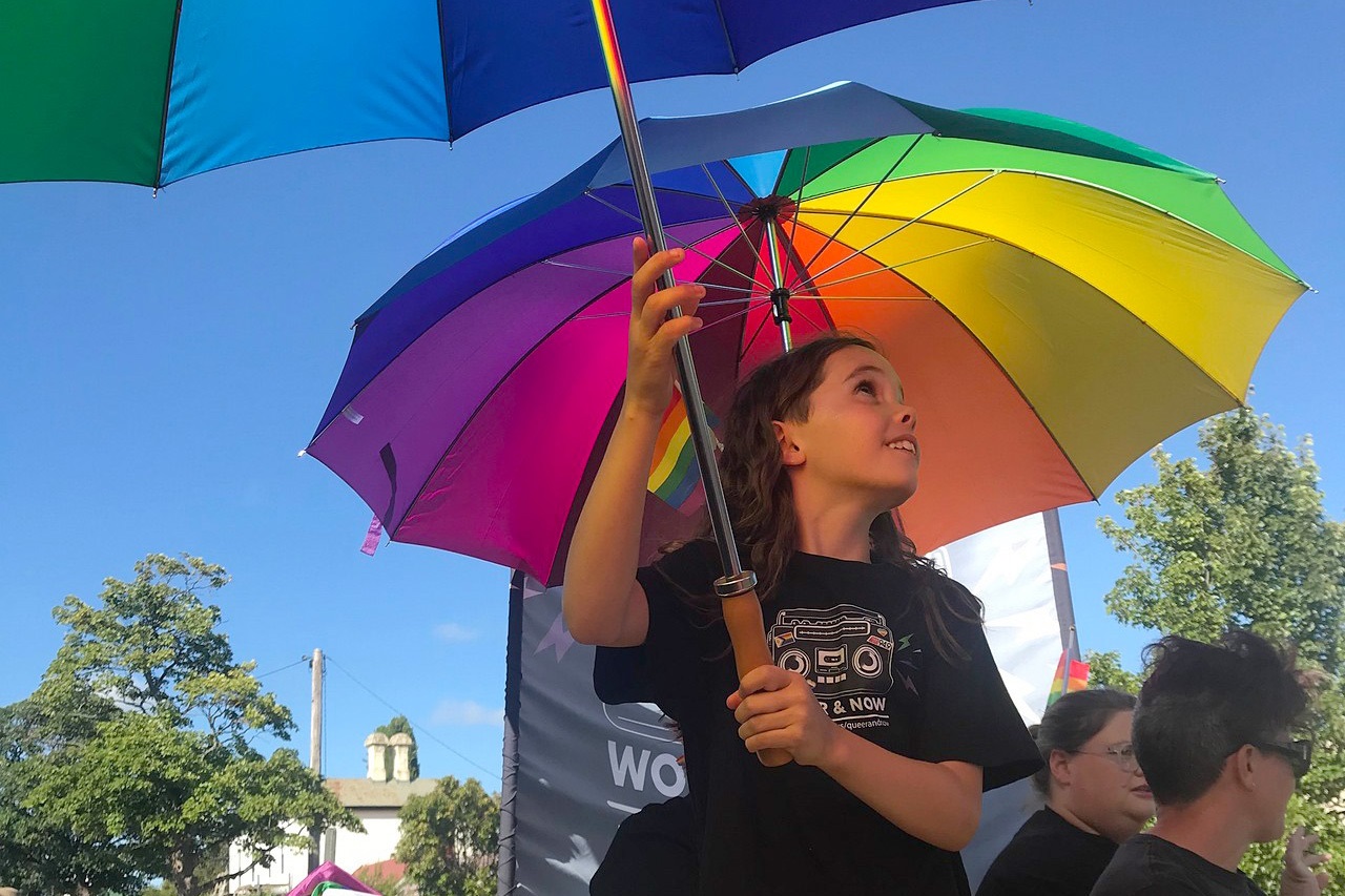 A girl holds open a rainbow umbrella