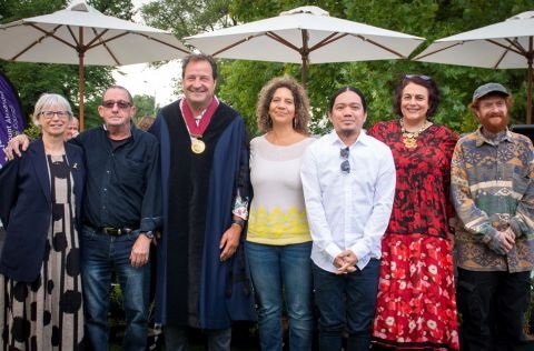 Seven people standing in front of three umbrellas at new citizenship ceremony. 