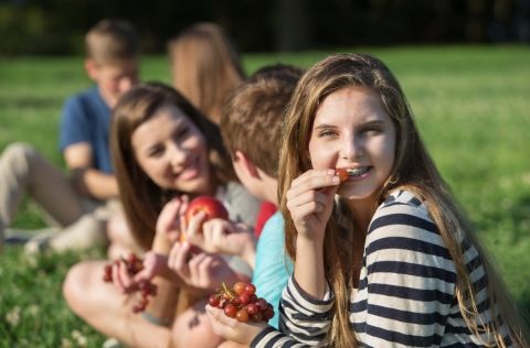 Five teenagers sitting on the grass outside eating fruit 
